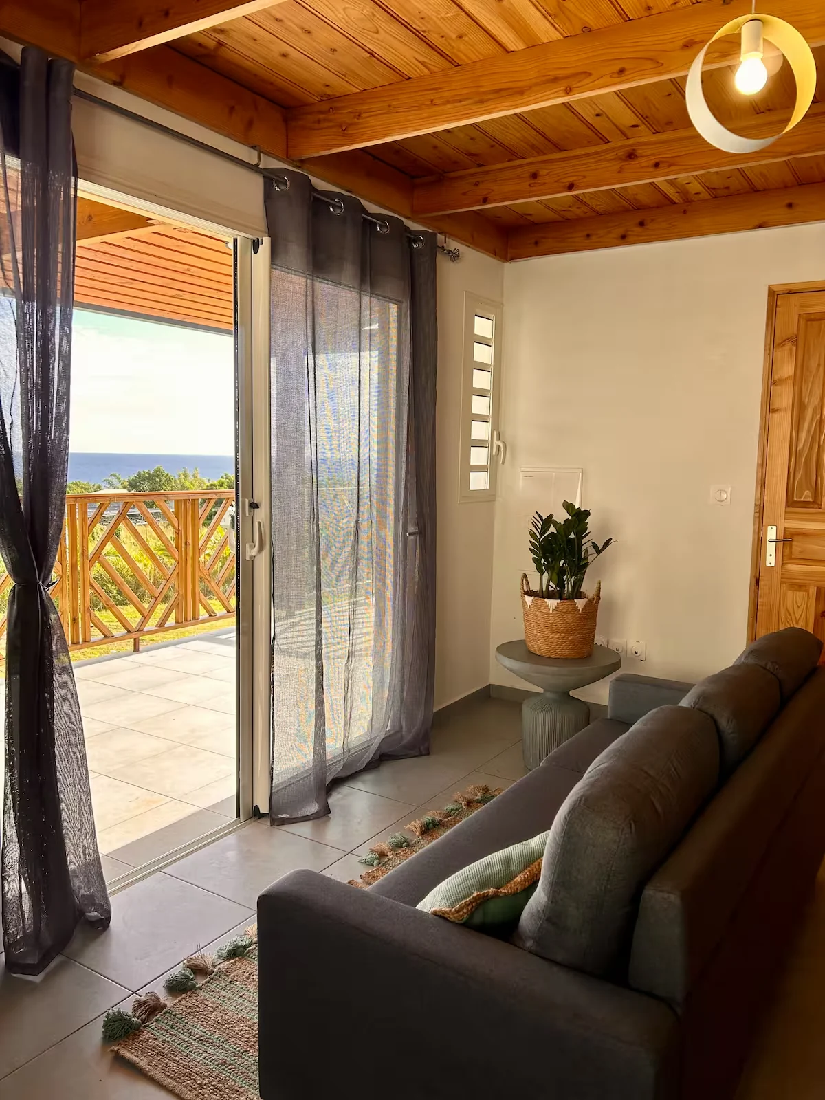 Séjour Émeraude ouvert sur la terrasse, canapé et plafond en bois